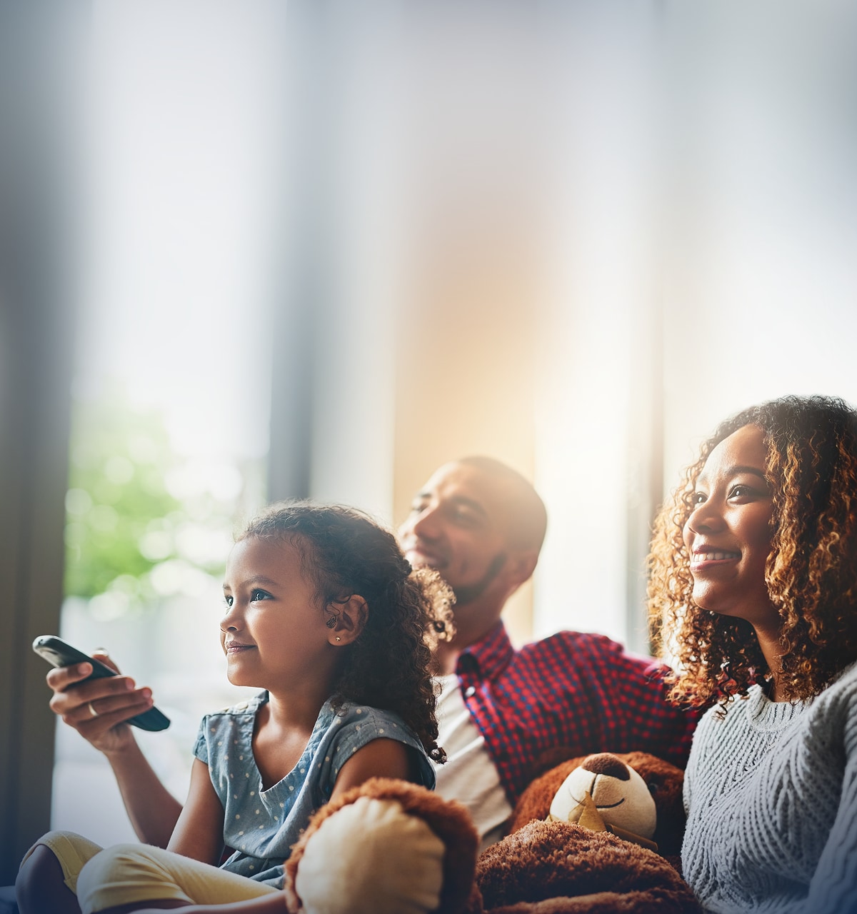 Smiling family watching television, and child holding a remote.