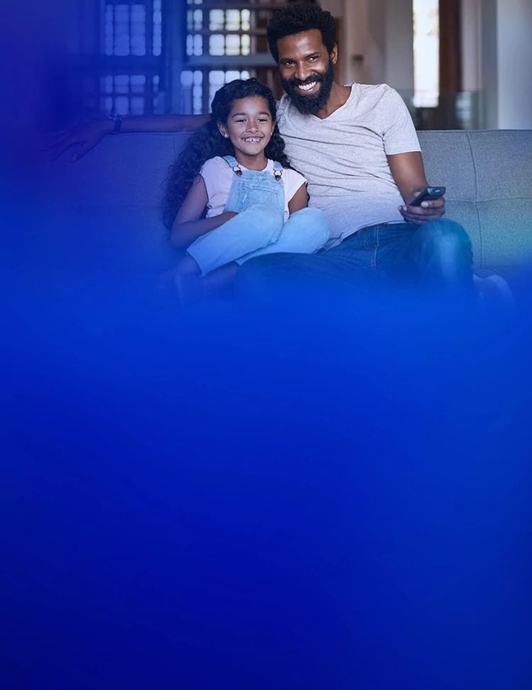A father and daughter are smiling while they sit together on a couch watching TV with U-verse