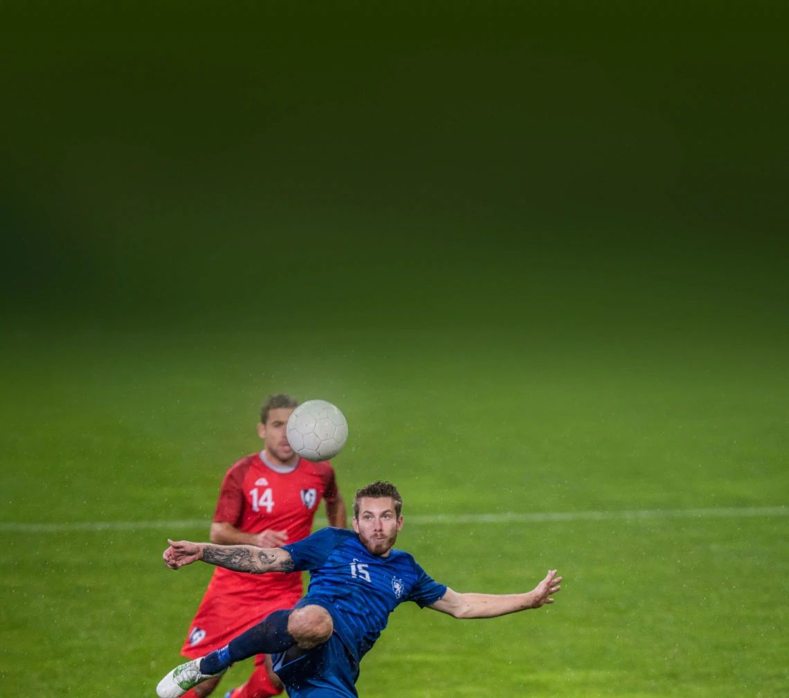 Soccer players in action with one player kicking a ball, representing sports coverage.
