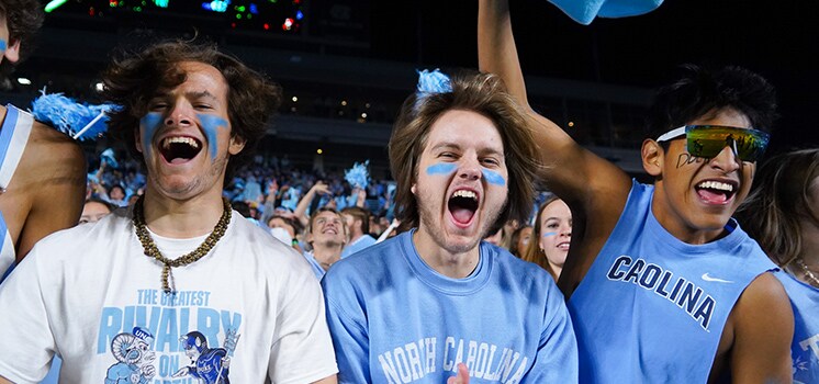 College fans in light blue Carolina shirts cheering in the stands.