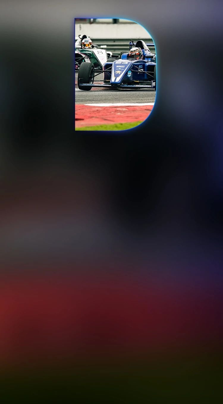 Formula One race car speeding on a racetrack with driver in full gear and another F1 car closely following in the background.