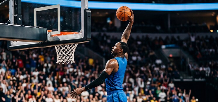 A basketball player in a light blue jersey driving to the hoop for a layup.
