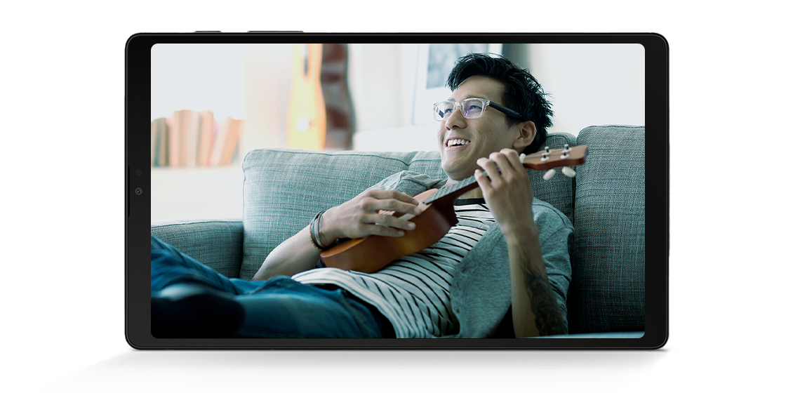 A man plays a ukulele while sitting on a couch