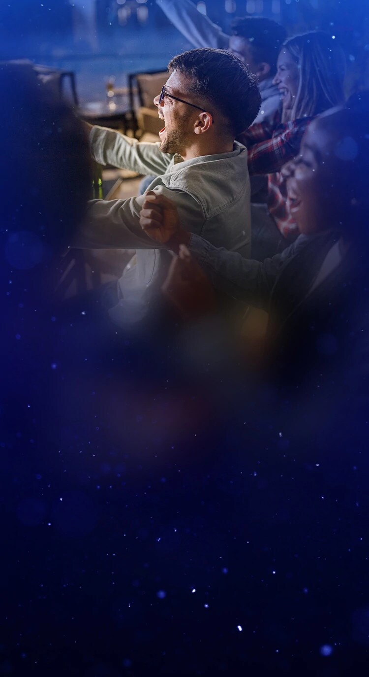 Group of friends cheering and watching TV together in a cozy, festive setting during the holidays.