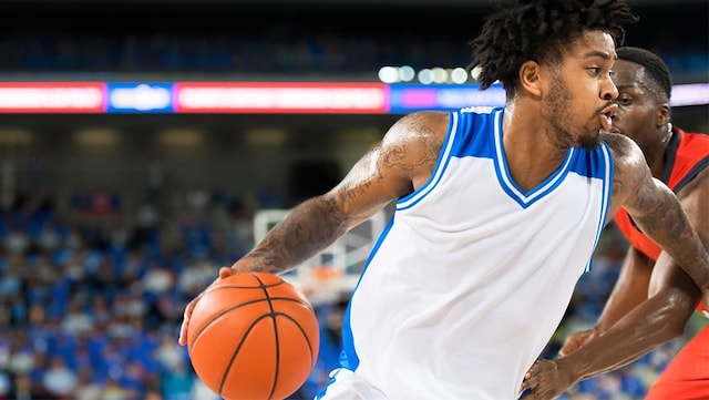 A college basketball player is moving with the basketball past an opposing guarding player