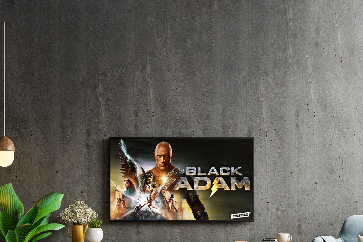 A Smart TV on a concrete wall above an entertainment center displays a title screen image for CINEMAX exclusive title Black Adam.