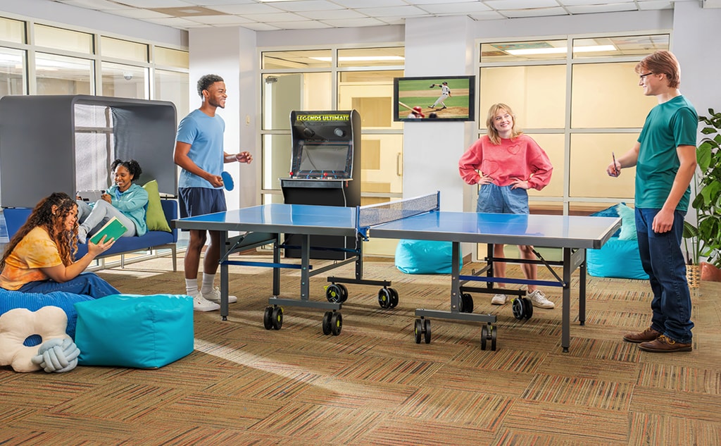 People playing ping pong in a rec center while others sit and read nearby.