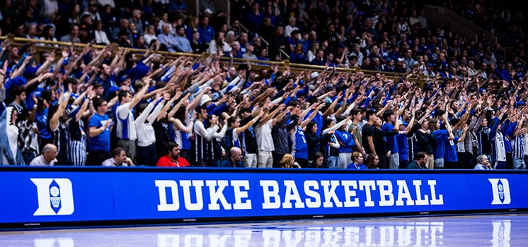 A Duke Basketball arena banner in front of a packed student section.