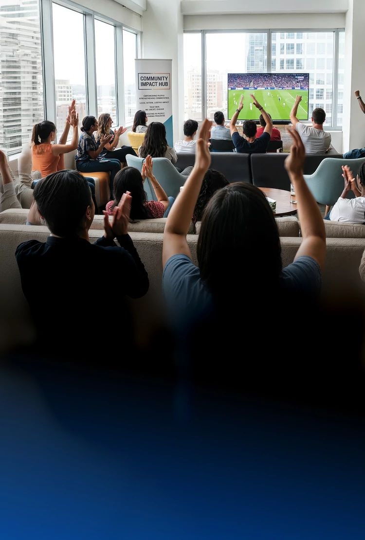 People gathered in a community space watching a soccer match on a TV and cheering together during a watch party
