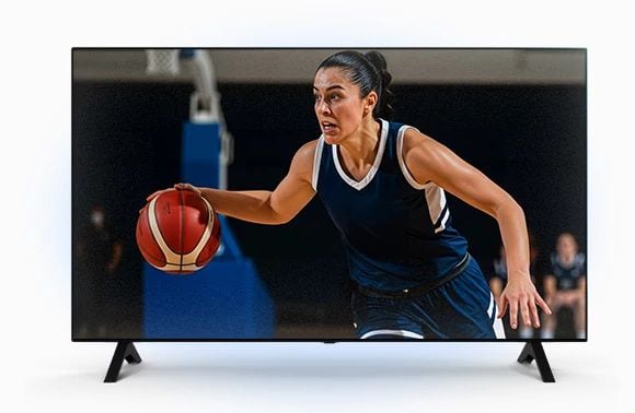 Female basketball player in a navy jersey dribbling the ball during a game, shown on a flat-screen TV display.